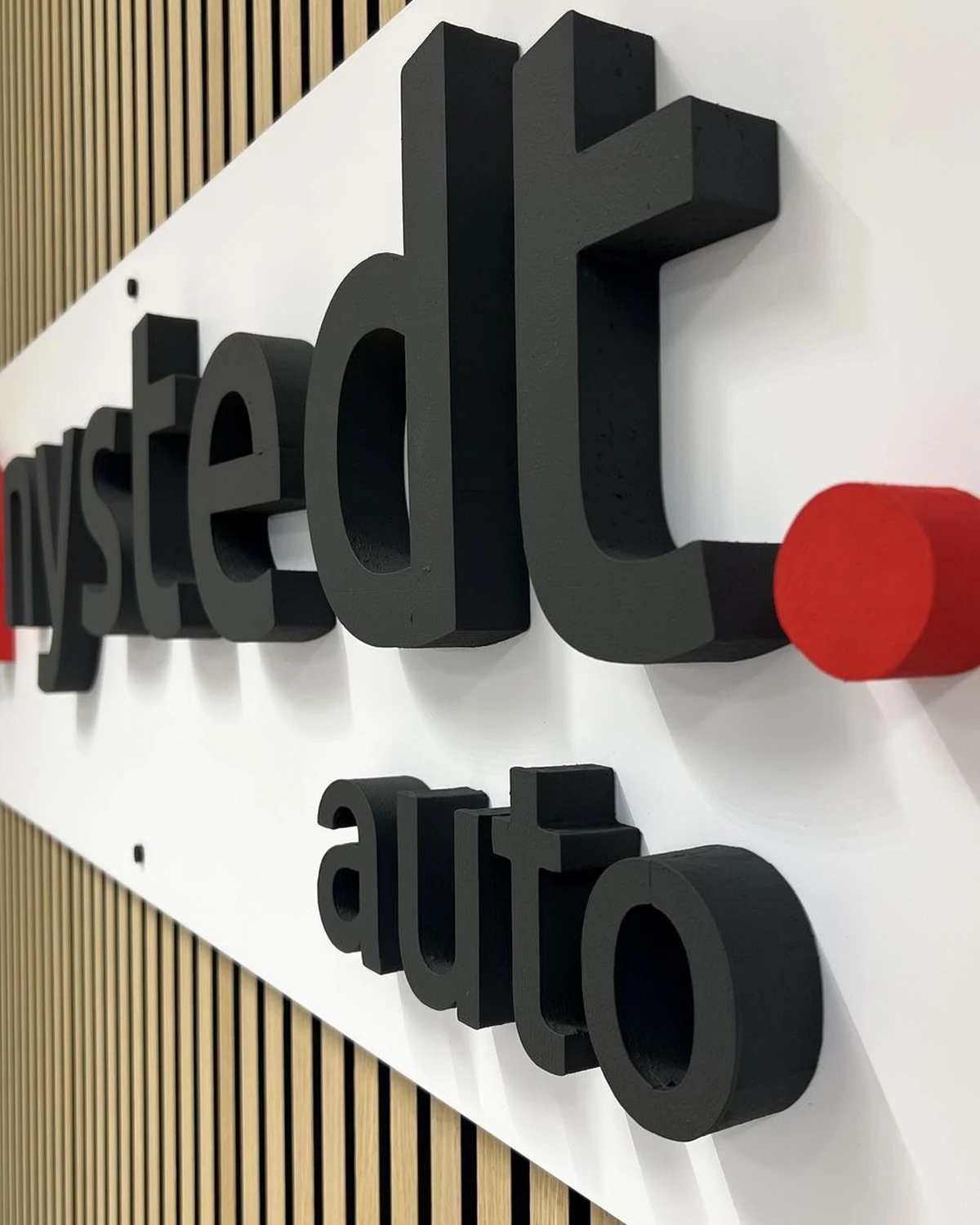 Autoliike Nystedtin kolmiulotteinen logo puisella rimaseinällä