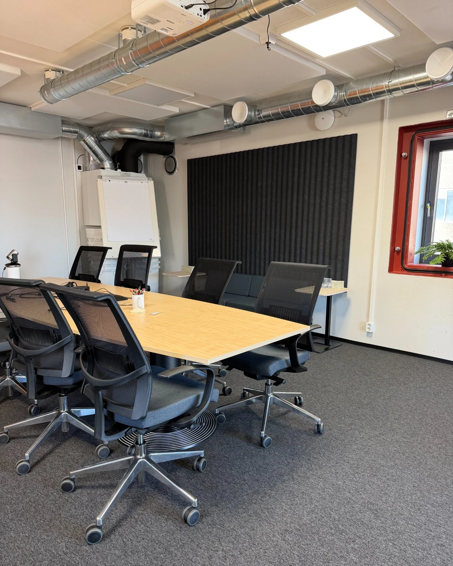 JTK Powerin neuvottelukäytössä oleva väestönsuoja, jossa on akustiikkapaneeleita seinällä ja katossa sekä harmaa tekstiilimatto.